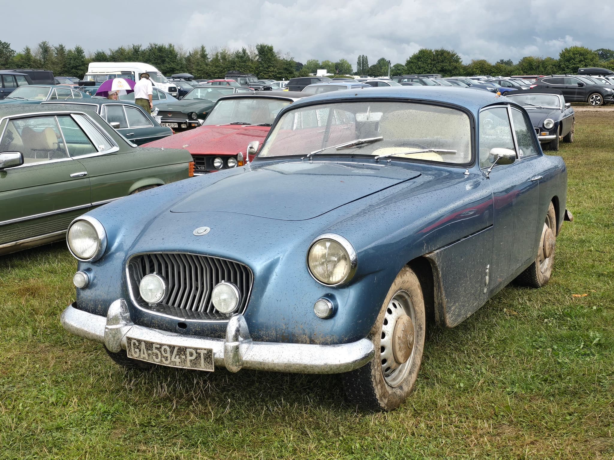 A dusty blue Bristol 406 saloon parked on grass among other classic cars.