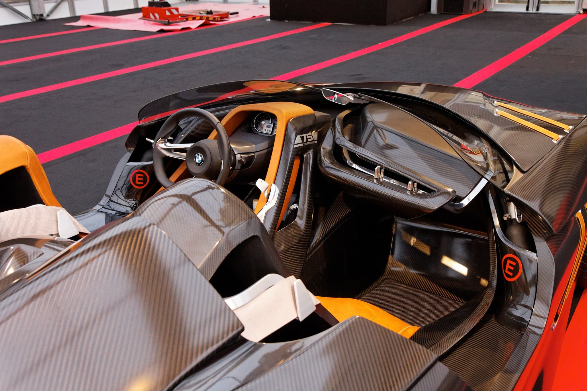 The carbon-fibre cockpit of the BMW 328 Hommage concept car, with a tan seat, a steering wheel and red extinguisher badges.