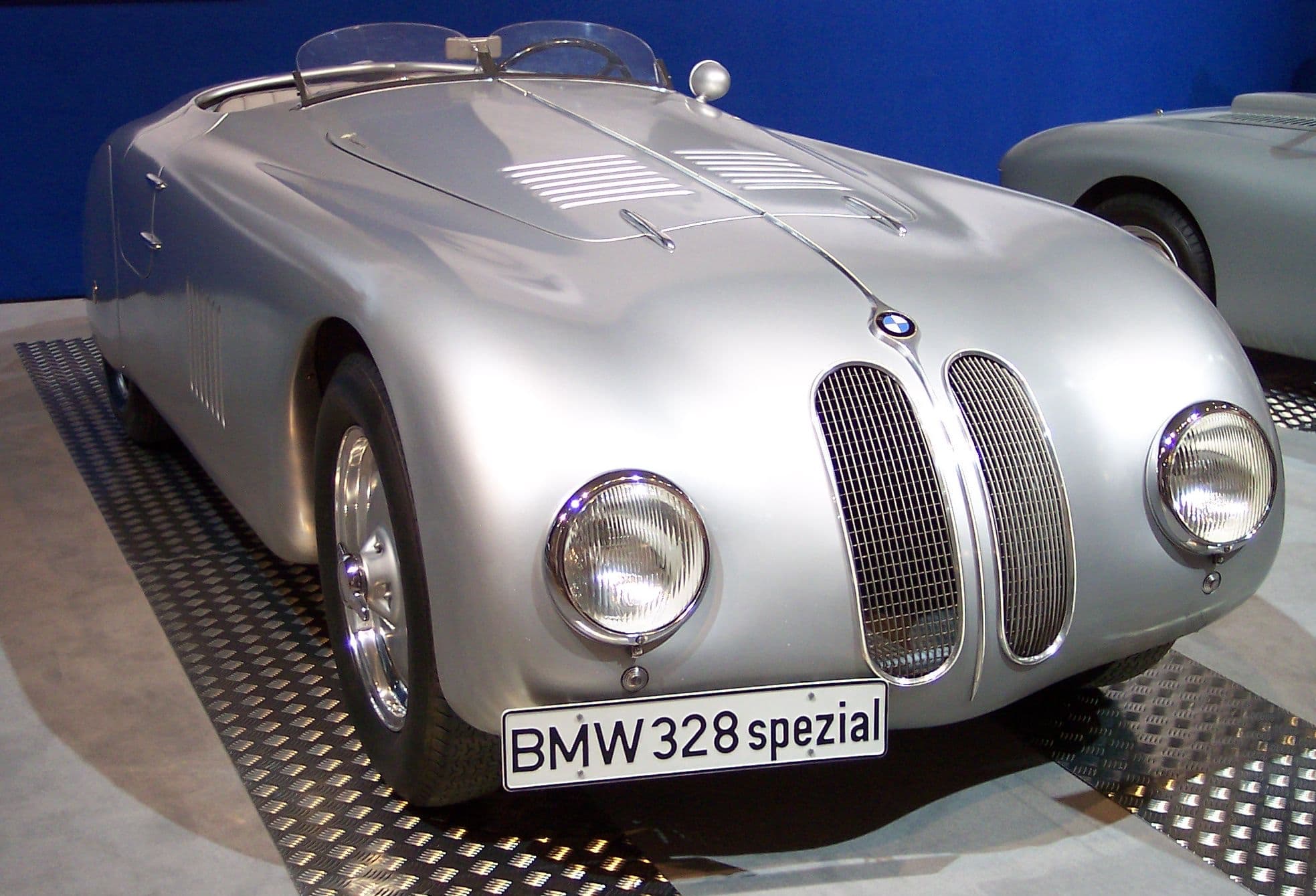 A silver streamlined BMW roadster on a show stand with a display plate reading 'BMW 328 spezial'.