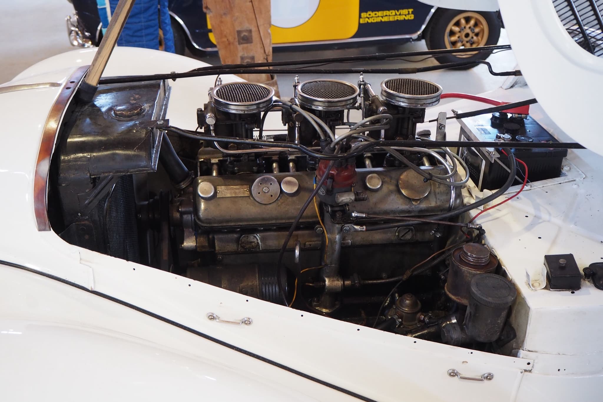 The engine bay of a white BMW 328: a six-cylinder engine with three downdraught carburettors under mesh filters. Opens a larger view