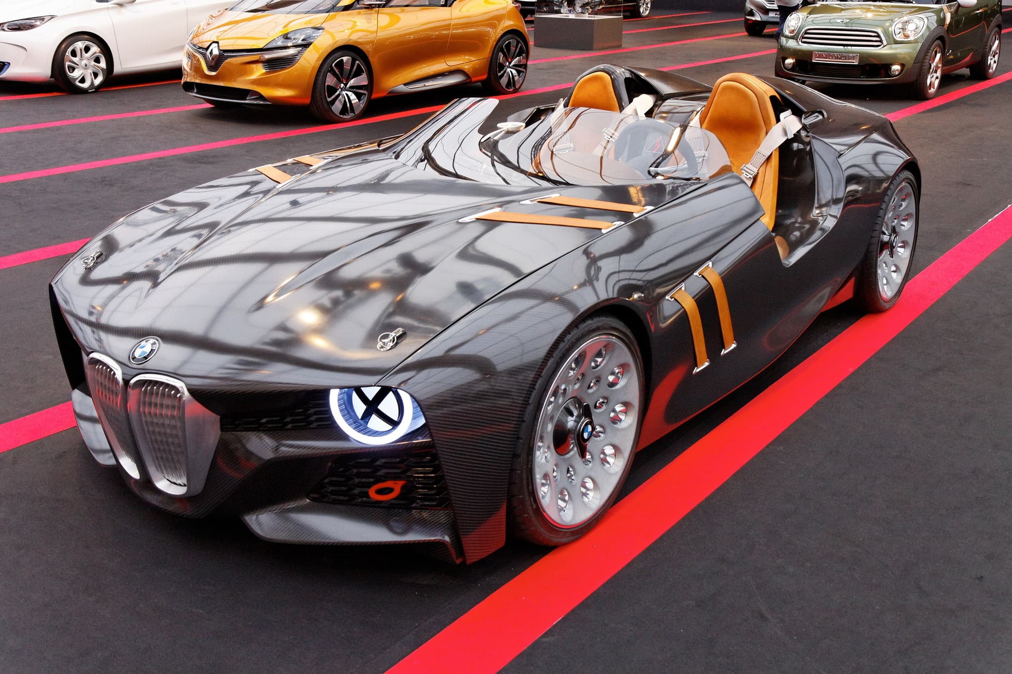 The carbon-fibre BMW 328 Hommage concept car with tan straps and X-lit headlamps on a striped show floor.
