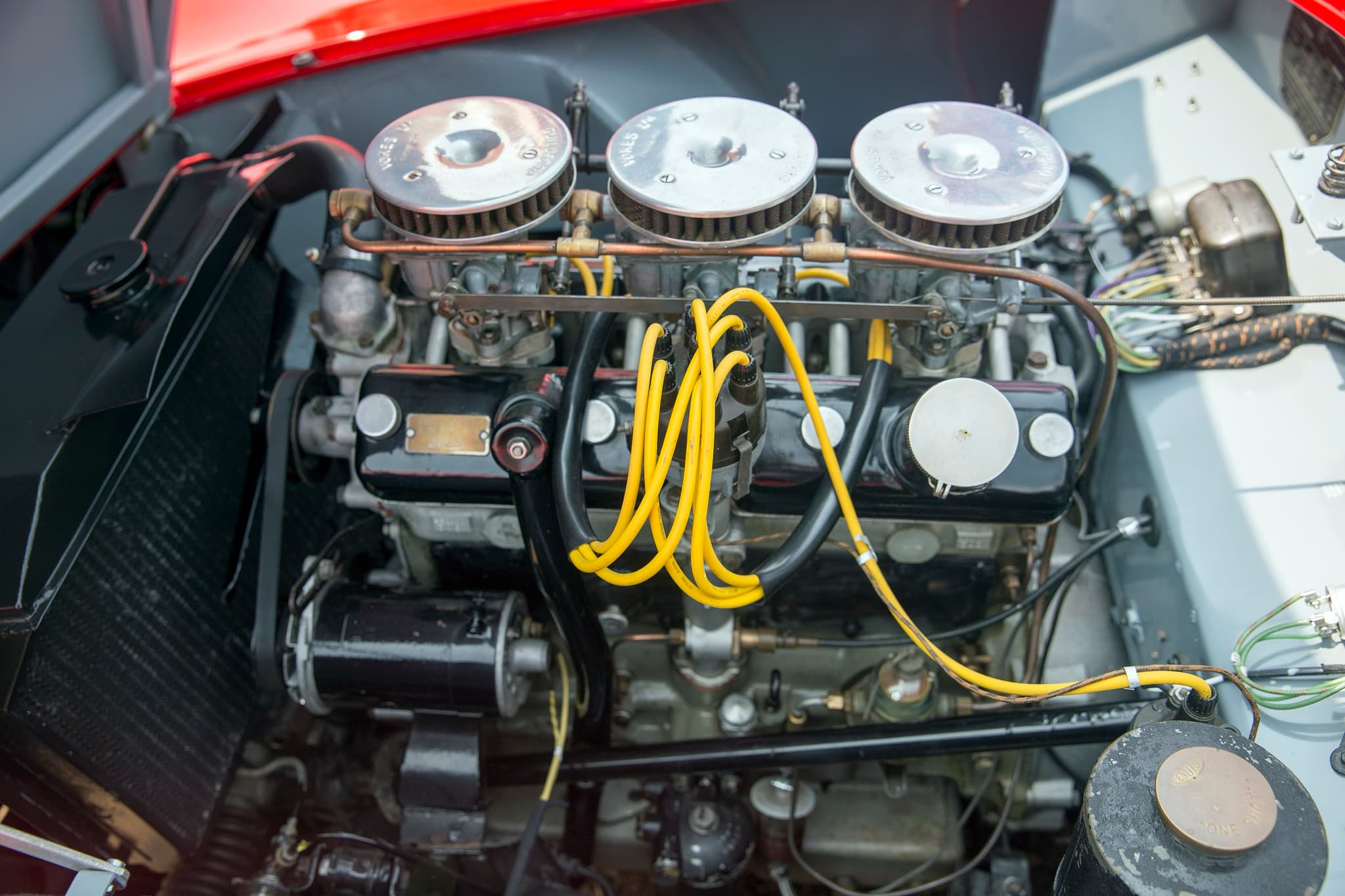 The side of a Bristol six-cylinder engine with three carburettors under chrome filters and yellow plug leads.