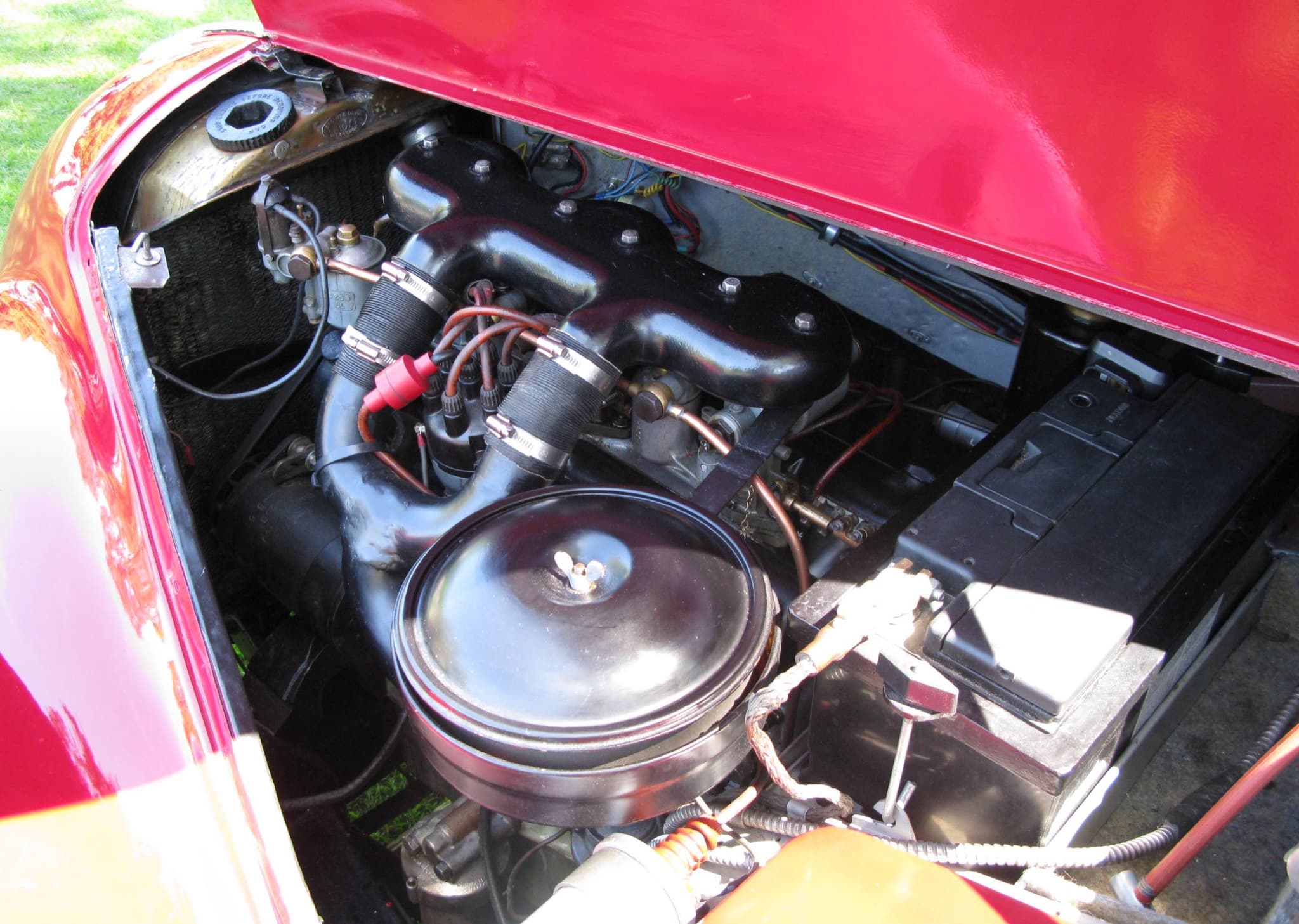The engine bay of a red Bristol 400: a six-cylinder engine with a large round air cleaner and three intake pipes.