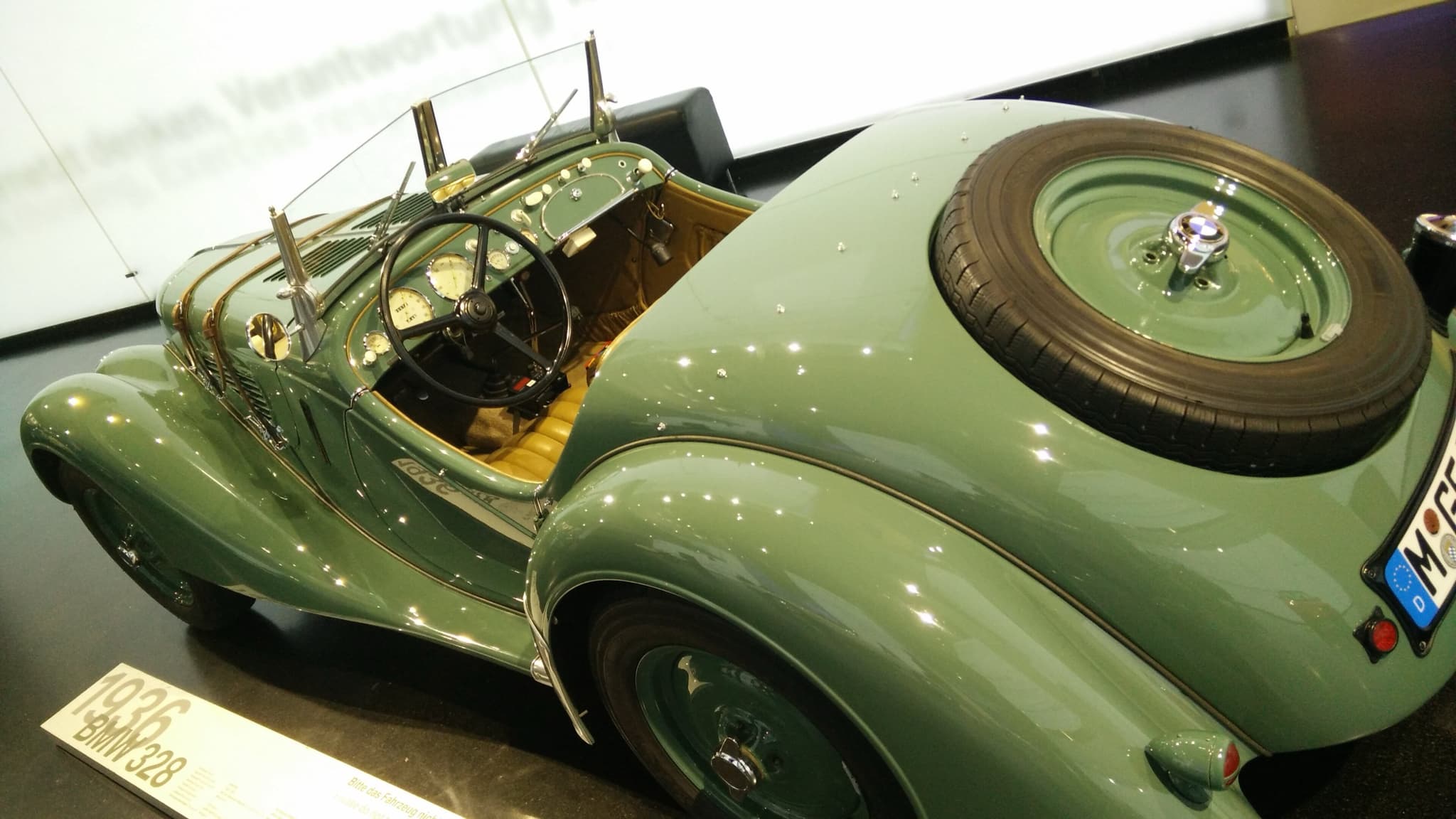 A green BMW 328 roadster seen from above at the left rear, with the spare wheel in its tail, the cockpit and the dials. Opens a larger view